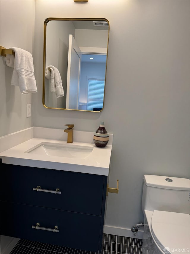 half bathroom with toilet, baseboards, vanity, and tile patterned floors