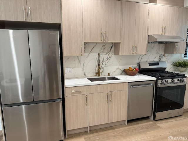 kitchen with light wood-style flooring, appliances with stainless steel finishes, under cabinet range hood, light brown cabinets, and a sink