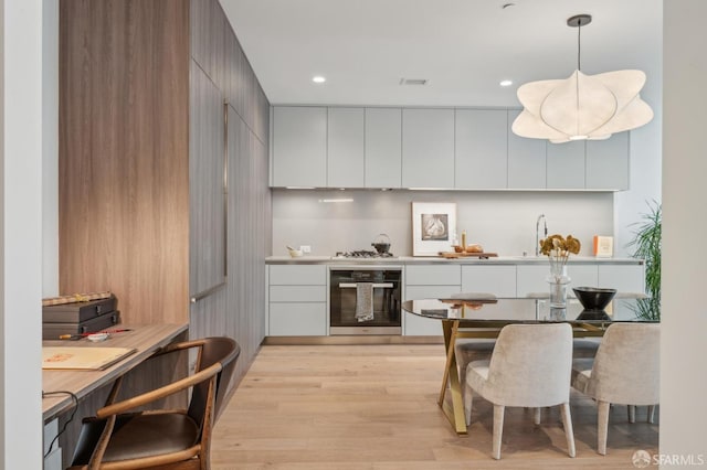 kitchen with light countertops, visible vents, light wood finished floors, modern cabinets, and wall oven