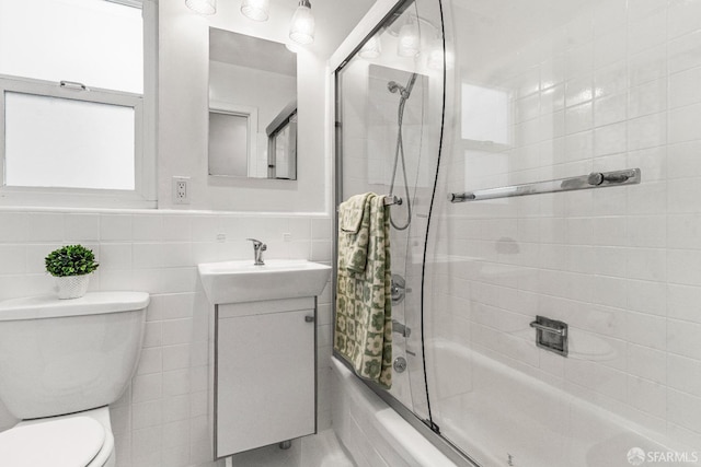 bathroom with toilet, combined bath / shower with glass door, tile walls, and vanity