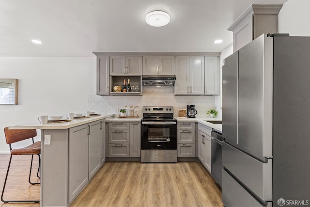 kitchen with under cabinet range hood, appliances with stainless steel finishes, a peninsula, and gray cabinetry