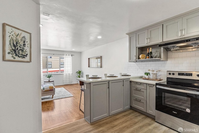 kitchen with a peninsula, under cabinet range hood, stainless steel range with electric cooktop, and gray cabinetry