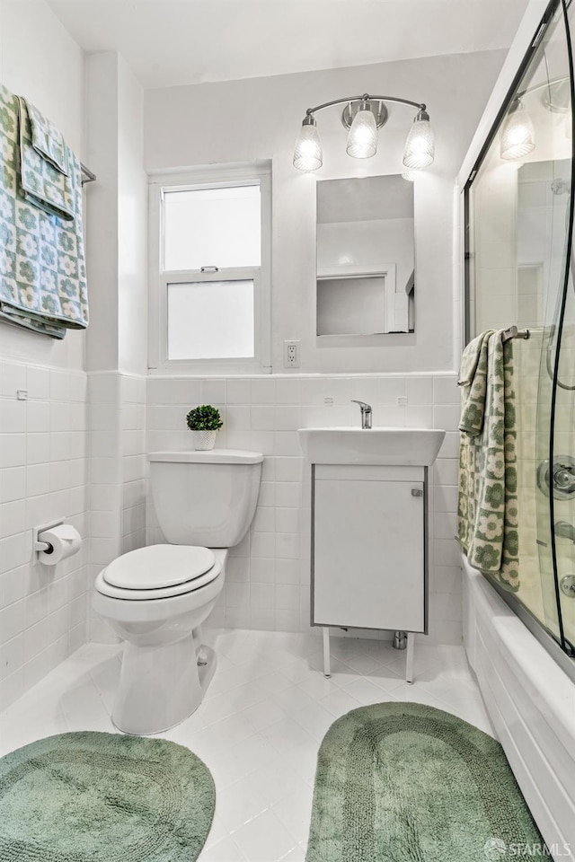 bathroom featuring wainscoting, toilet, combined bath / shower with glass door, vanity, and tile walls