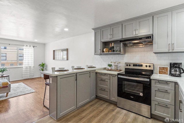 kitchen featuring light wood finished floors, a peninsula, gray cabinets, stainless steel range with electric cooktop, and under cabinet range hood