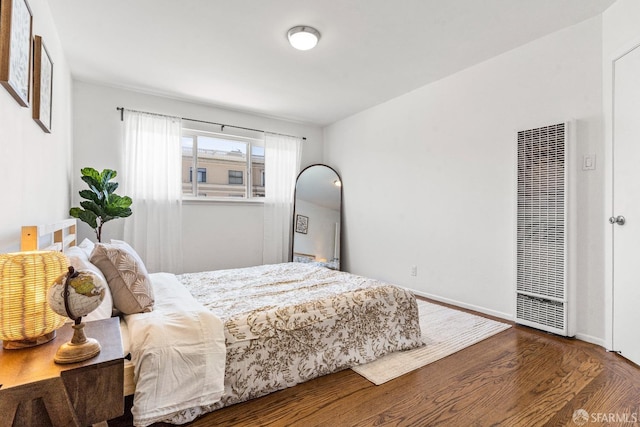 bedroom featuring a heating unit, baseboards, and wood finished floors