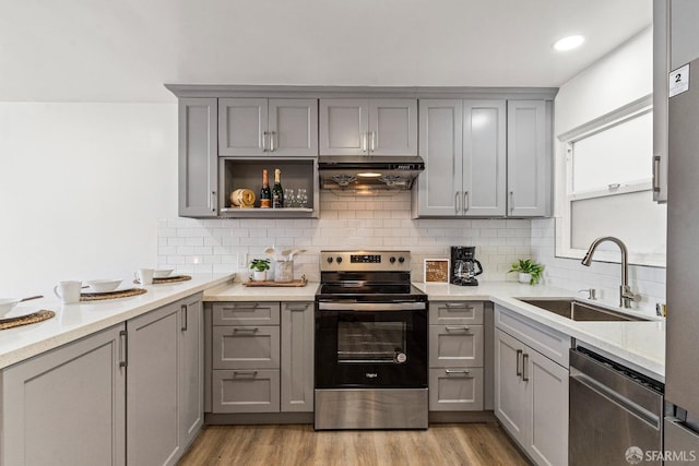 kitchen with appliances with stainless steel finishes, gray cabinetry, light wood-type flooring, under cabinet range hood, and a sink