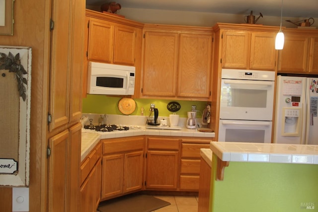 kitchen featuring light tile patterned floors, hanging light fixtures, white appliances, and tile counters