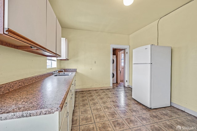 kitchen featuring white cabinets, white fridge, stacked washer / dryer, and sink