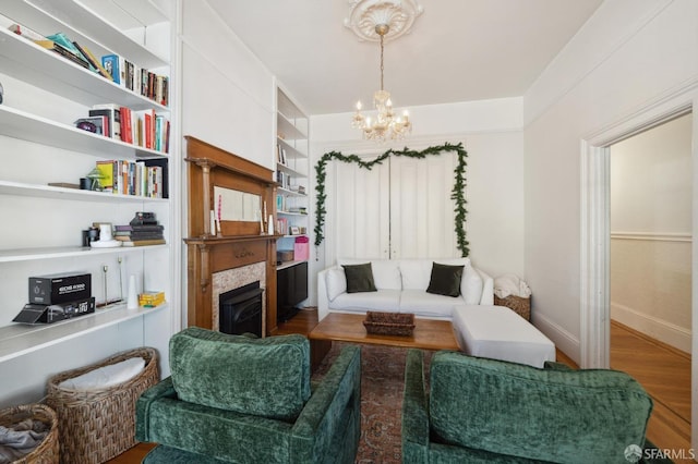 living room featuring a tiled fireplace, built in features, a notable chandelier, and hardwood / wood-style flooring