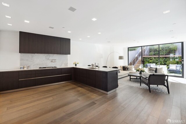 kitchen featuring dark brown cabinets, light hardwood / wood-style floors, tasteful backsplash, gas cooktop, and a wall of windows