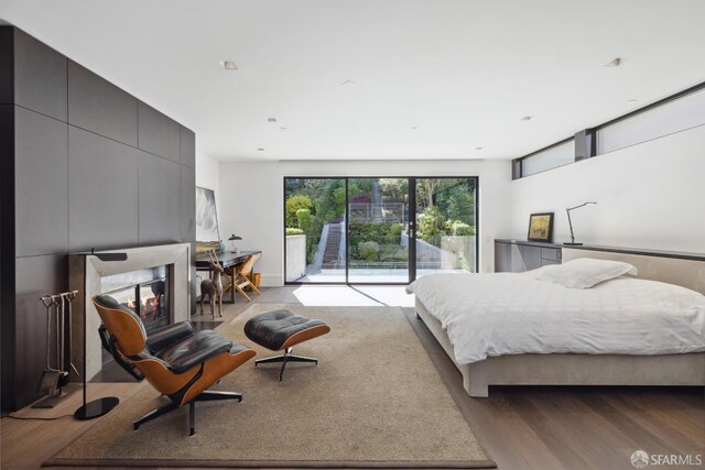 bedroom featuring access to outside, a multi sided fireplace, and wood-type flooring