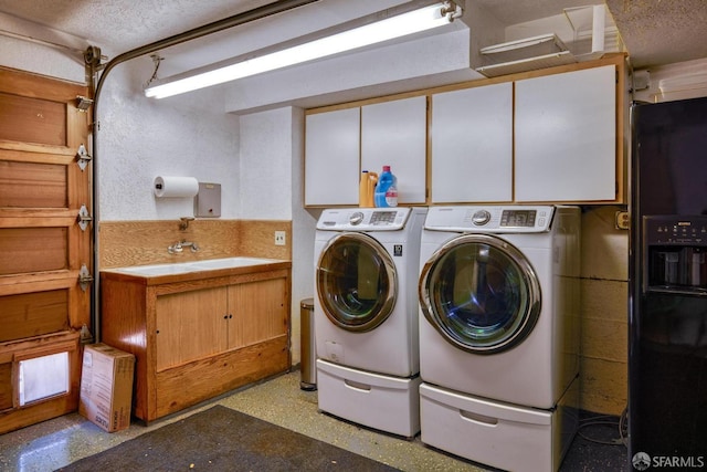 clothes washing area with cabinets, sink, washing machine and clothes dryer, and a textured ceiling