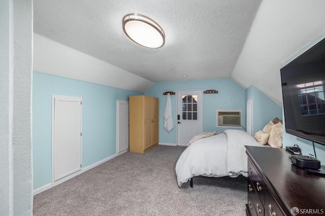 bedroom with a textured ceiling, vaulted ceiling, light carpet, and an AC wall unit