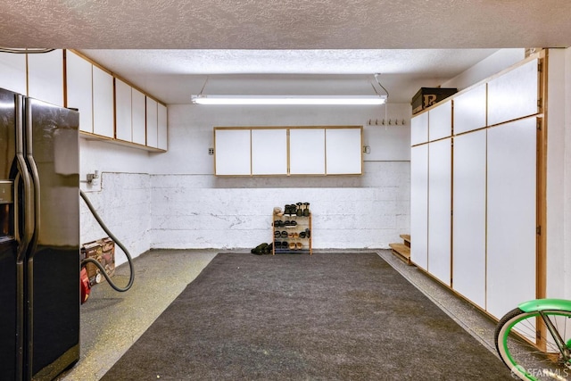 basement with a textured ceiling and black fridge