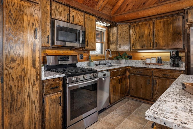 kitchen featuring stainless steel appliances, light stone countertops, sink, and lofted ceiling