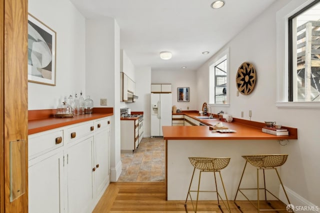 kitchen with white cabinets, a breakfast bar, range with gas cooktop, and white fridge with ice dispenser