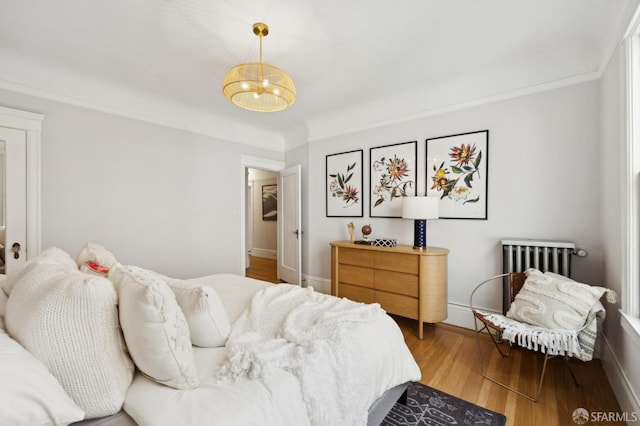 bedroom featuring wood finished floors, baseboards, radiator heating unit, crown molding, and a chandelier