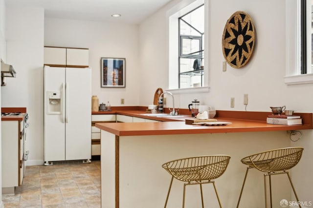 kitchen with a peninsula, a sink, stove, white cabinets, and white fridge with ice dispenser