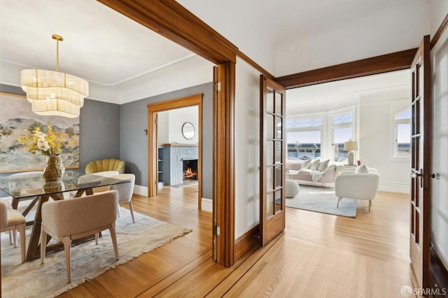 dining space with a tiled fireplace, an inviting chandelier, baseboards, and light wood finished floors