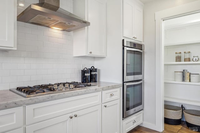 kitchen with tasteful backsplash, wall chimney range hood, white cabinets, and appliances with stainless steel finishes