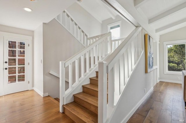 stairs with wood-type flooring and vaulted ceiling with beams