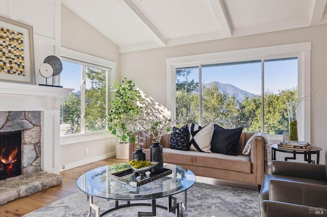 living room featuring a mountain view, a stone fireplace, lofted ceiling with beams, and hardwood / wood-style flooring