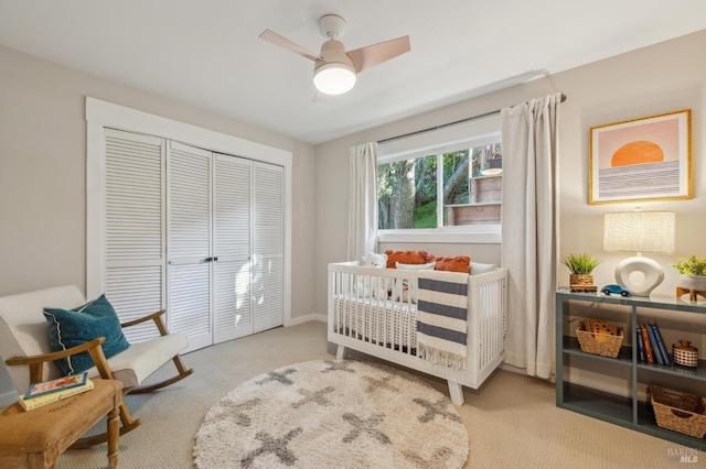 carpeted bedroom with ceiling fan, a closet, and a crib