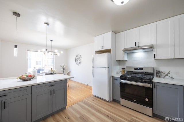 kitchen with stainless steel gas range, freestanding refrigerator, under cabinet range hood, and gray cabinets
