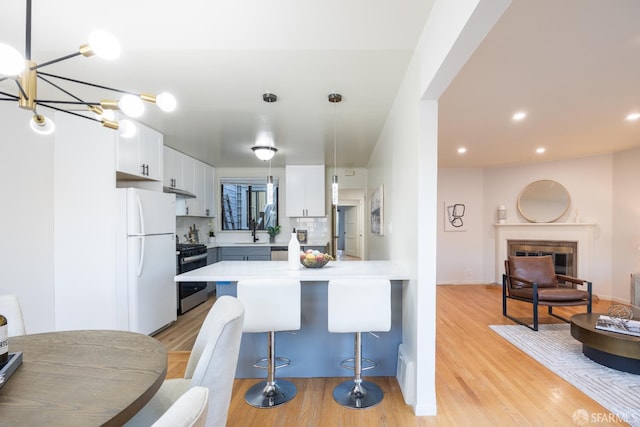 kitchen with stainless steel range with gas cooktop, freestanding refrigerator, a kitchen breakfast bar, light wood-style flooring, and a peninsula