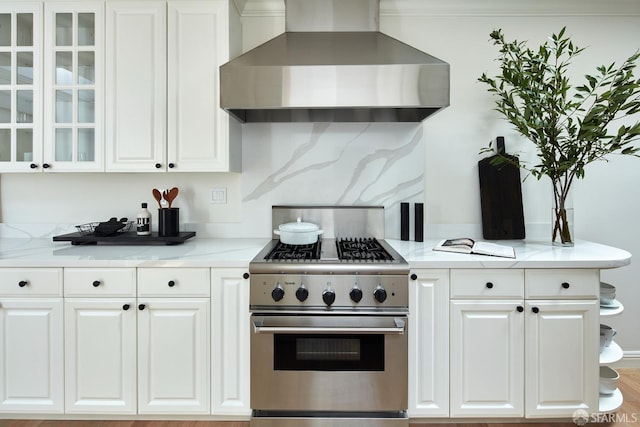 kitchen with high end stainless steel range oven, wall chimney range hood, and white cabinets
