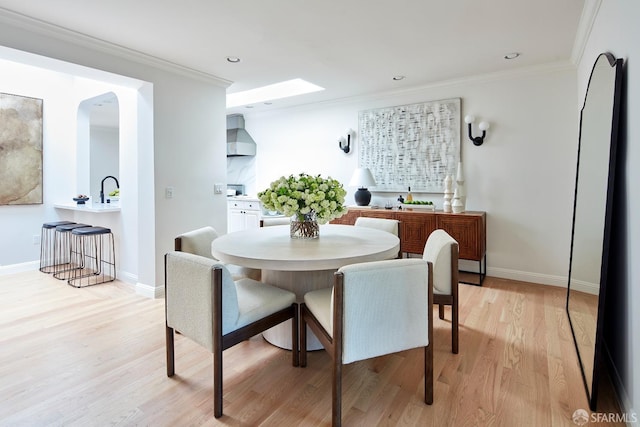 dining area featuring light wood finished floors, ornamental molding, baseboards, recessed lighting, and arched walkways