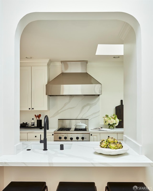 kitchen with wall chimney range hood, arched walkways, a breakfast bar, white cabinets, and decorative backsplash