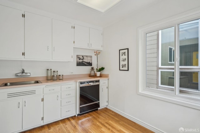 kitchen featuring a sink, light wood finished floors, dishwasher, light countertops, and white cabinetry