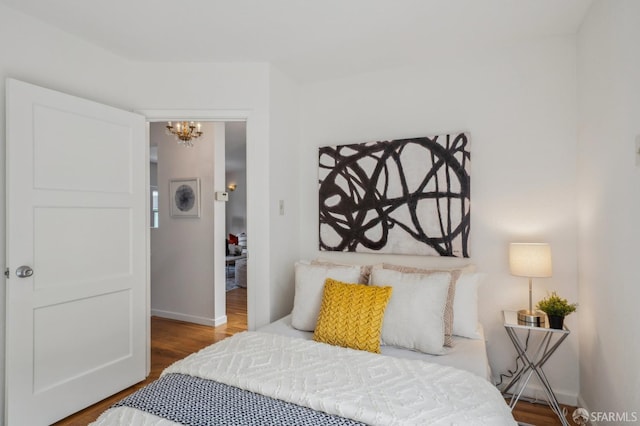 bedroom with baseboards, an inviting chandelier, and wood finished floors
