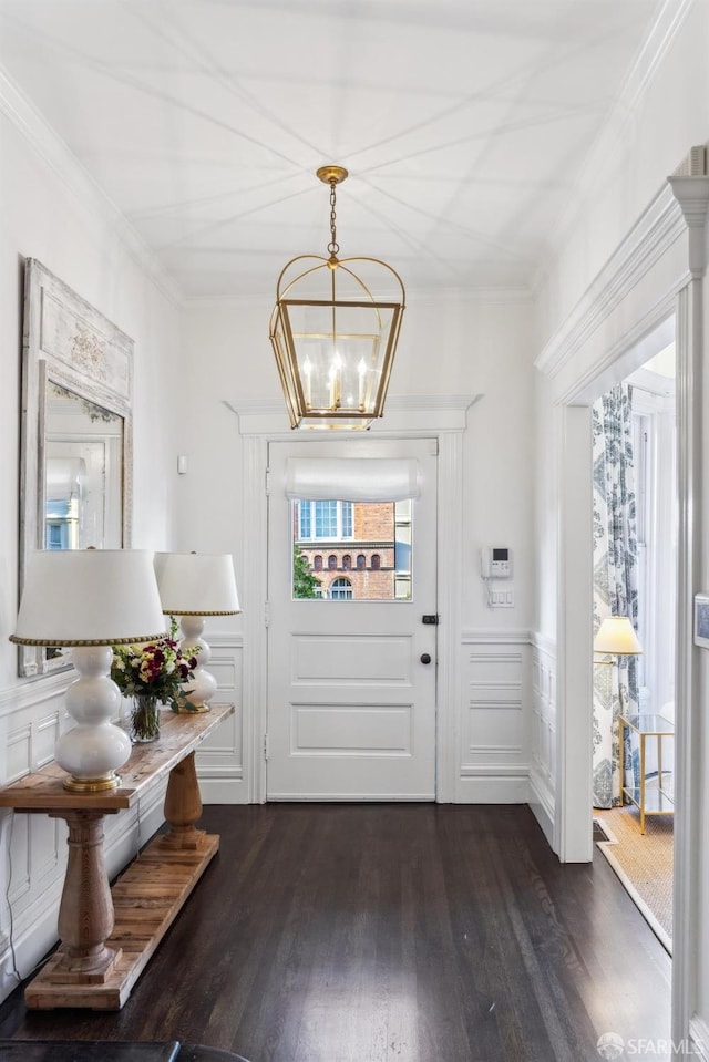 entryway with ornamental molding, dark wood-type flooring, wainscoting, and a notable chandelier