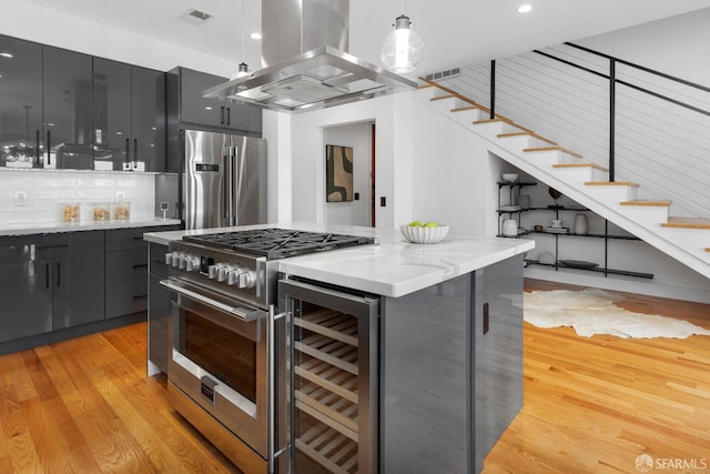 kitchen featuring appliances with stainless steel finishes, light wood-type flooring, island range hood, wine cooler, and hanging light fixtures