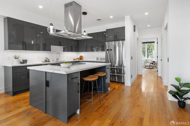 kitchen featuring stainless steel appliances, island exhaust hood, pendant lighting, light hardwood / wood-style floors, and a kitchen island