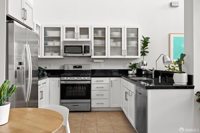 kitchen featuring dark stone counters, white cabinets, sink, light tile patterned flooring, and stainless steel appliances