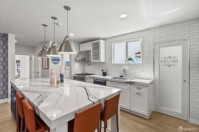 kitchen with a sink, light wood-style floors, a kitchen island, a breakfast bar, and white cabinets