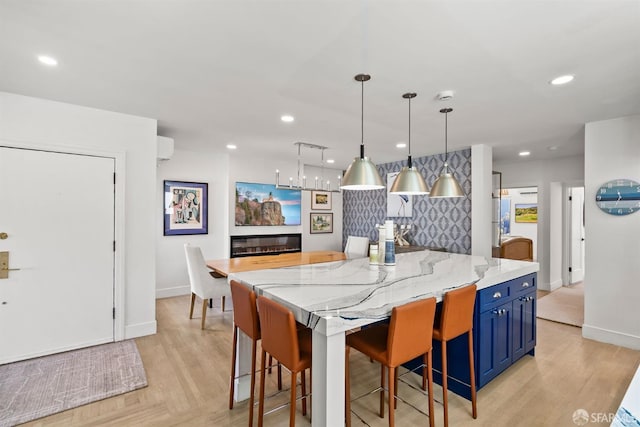 kitchen featuring blue cabinets, baseboards, a large island, light wood-style flooring, and light stone countertops