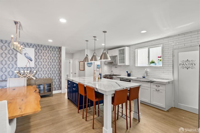 kitchen featuring a sink, a kitchen island, white cabinetry, wallpapered walls, and light wood-type flooring
