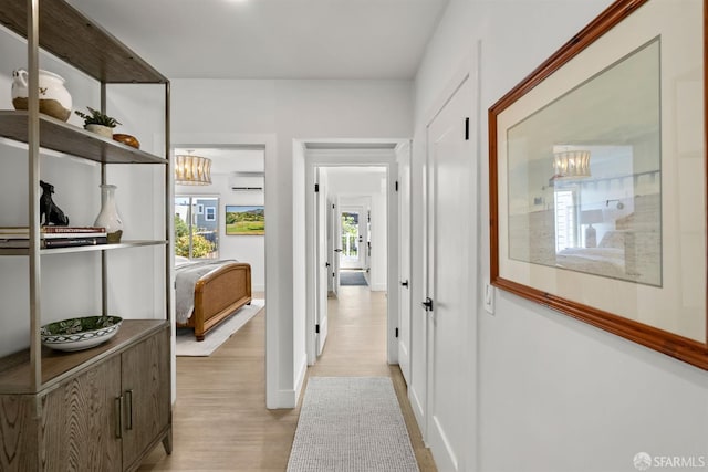 hallway featuring a wall unit AC, a chandelier, light wood-type flooring, and baseboards