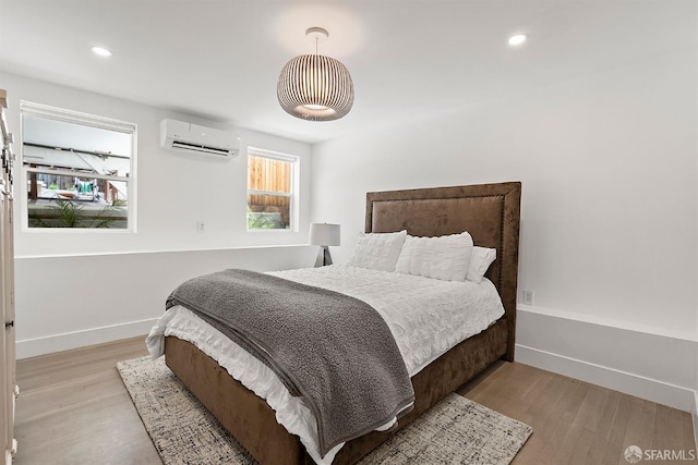 bedroom featuring a wall mounted AC, light wood-style flooring, baseboards, and recessed lighting