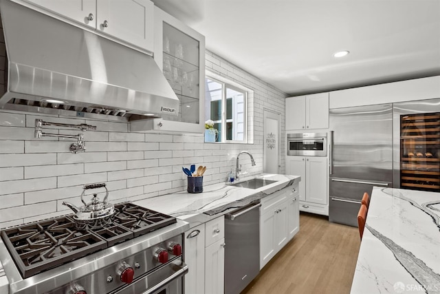 kitchen with appliances with stainless steel finishes, under cabinet range hood, a sink, white cabinets, and tasteful backsplash