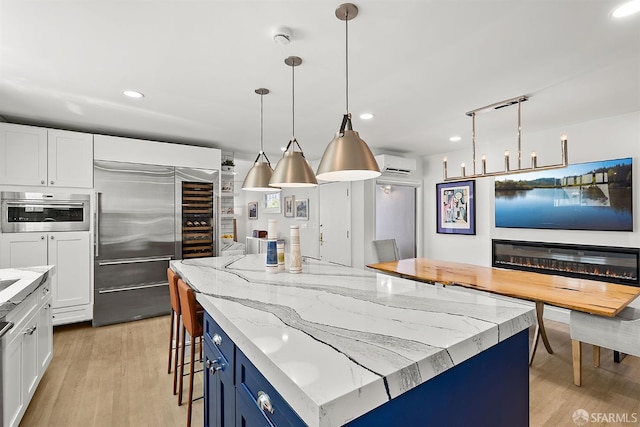 kitchen with appliances with stainless steel finishes, an AC wall unit, light wood finished floors, white cabinetry, and recessed lighting
