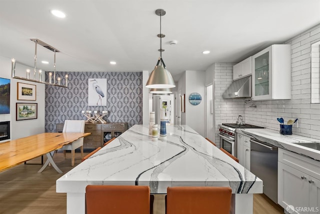 kitchen featuring stainless steel appliances, under cabinet range hood, a center island, white cabinetry, and light stone counters