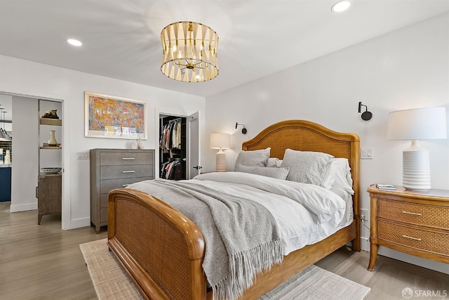 bedroom featuring light wood-style flooring, a chandelier, a walk in closet, a closet, and recessed lighting