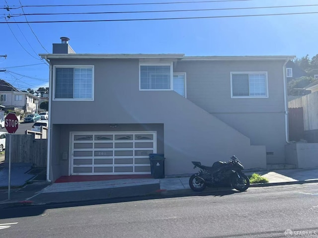 view of front of house featuring fence, a chimney, an attached garage, and stucco siding