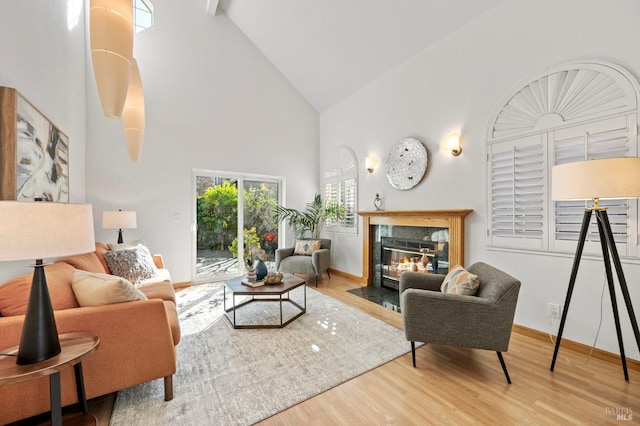 living room featuring high vaulted ceiling, a fireplace, baseboards, and wood finished floors