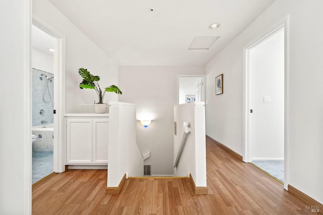 hall with light wood-type flooring, attic access, visible vents, and an upstairs landing